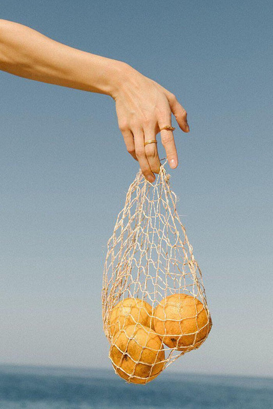 Hand with rings and a net of oranges against blue skies